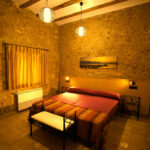 "Dormitori amb llit doble, parets de pedra i llum càlida."