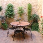 "Terrassa amb taula rodona, cadires de ferro i paret decorada amb plantes."